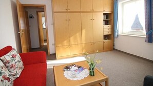 Ein Zimmer mit einem roten Sofa, einem Holzschrank, einem kleinen Tisch mit einer Vase und einem Fenster mit Vorhängen.