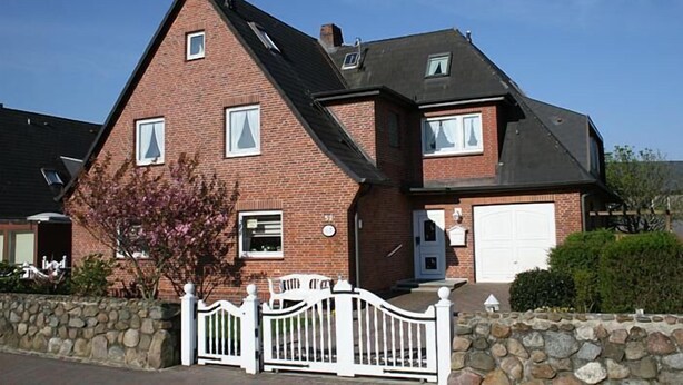 Une maison à deux étages, construite en briques, avec une clôture blanche, un garage et un petit jardin.