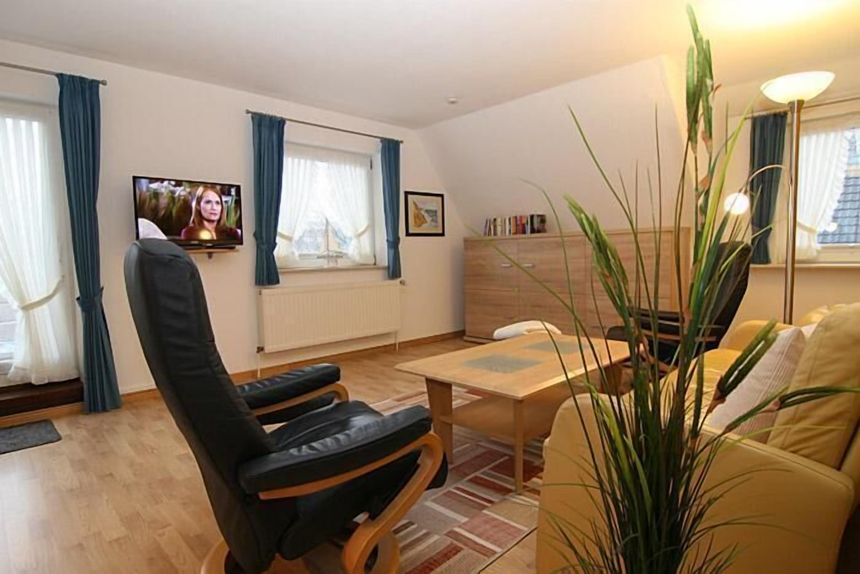 Uma sala de estar com sofá, mesa de centro, televisão e planta.