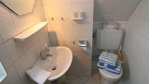 Un baño pequeño con lavamanos, inodoro y estantes de almacenamiento.