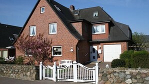 Una casa de ladrillo de dos pisos con cerca blanca, un garaje y un pequeño jardín.