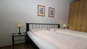 Un dormitorio con una cama, dos lámparas de noche, un armario de madera y dos cuadros en la pared.