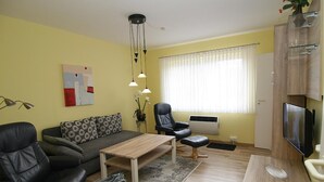 Una sala de estar con un sofá, dos sillones, una mesa de centro, un televisor y una ventana con cortinas.