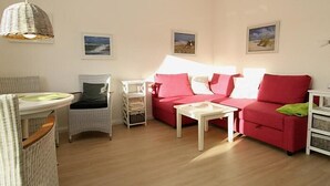 Een woonkamer met een rode bank, een witte salontafel, rieten stoelen en een hanglamp.