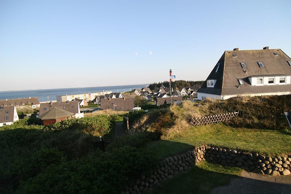 A coastal residential area with houses, a lighthouse, and a clear view of the sea.