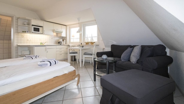 Ein kompakter, moderner Raum mit Bett, Sofa, kleinem Tisch und Küchenzeile.