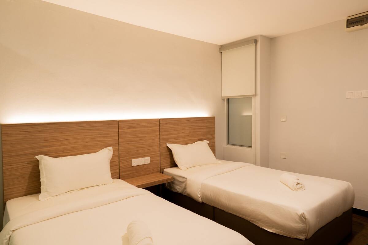 Ein Hotelzimmer mit zwei Einzelbetten, einem Holzkopfende, einem Nachttisch und einem Fenster mit Blick.