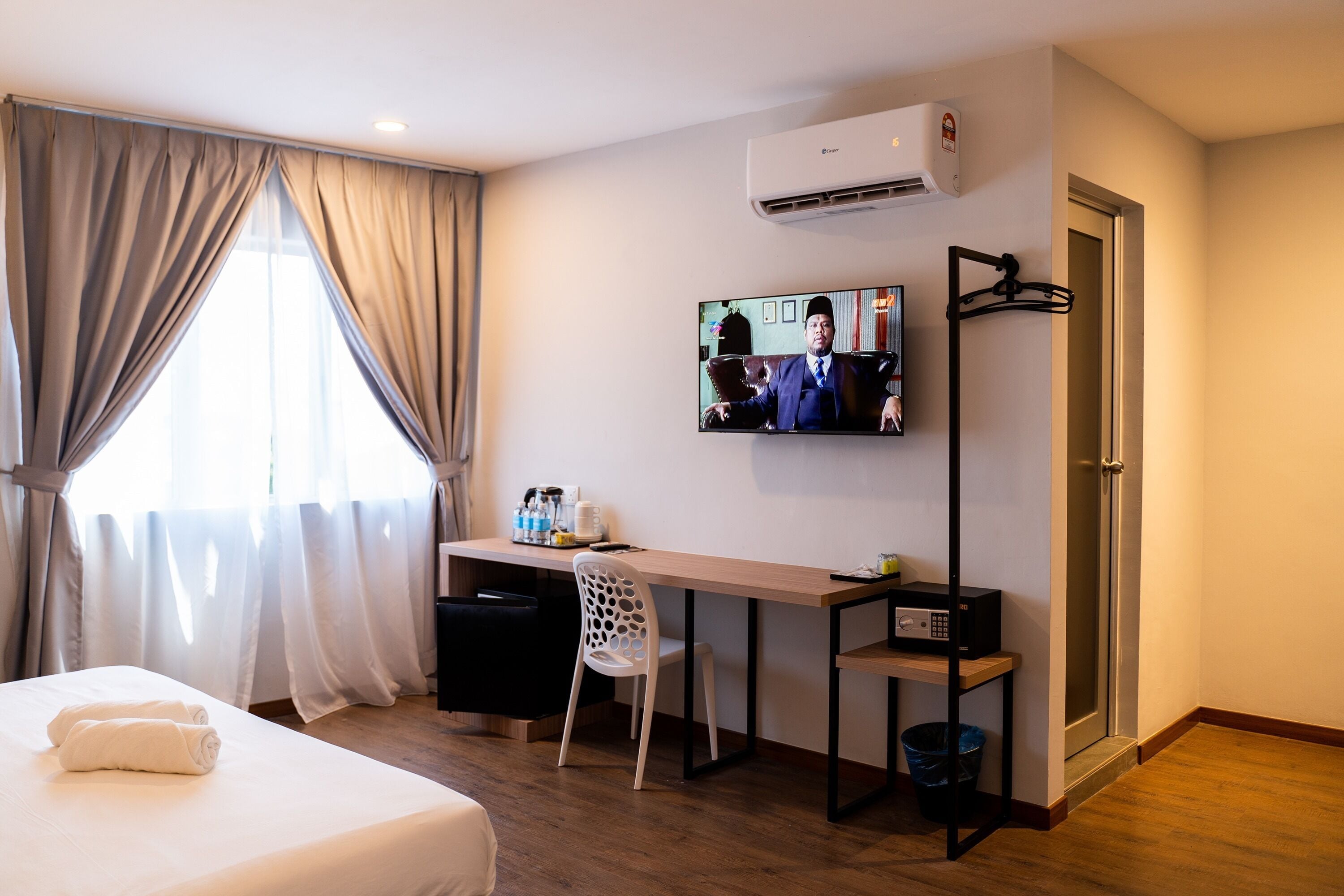 A hotel room with a bed, a desk, a chair, a TV, and a door.