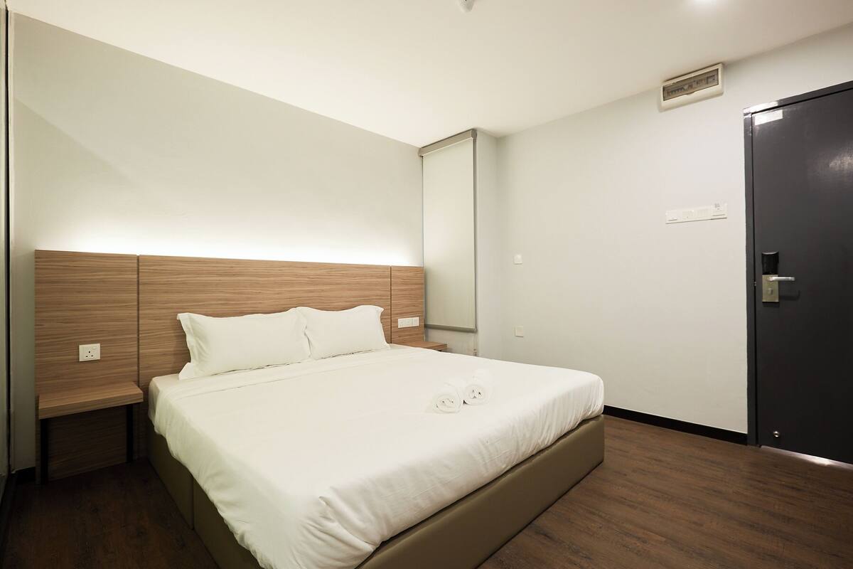 Ein modernes Hotelzimmer mit einem großen Bett, einem Holzkopfende, einem Nachttisch und einer dunklen Tür.