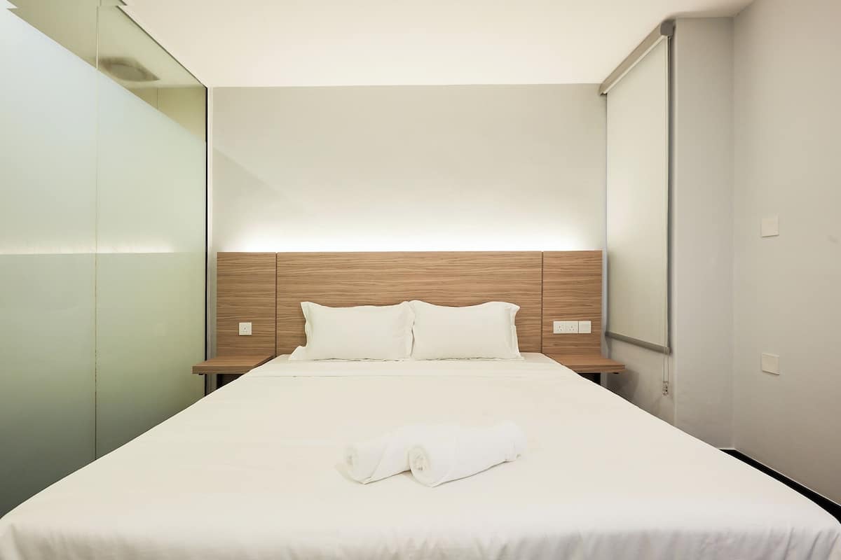 Ein Hotelzimmer mit einem großen Bett, einem hölzernen Kopfteil, weißer Bettwäsche und einem ordentlich gefalteten Handtuch auf dem Bett.
