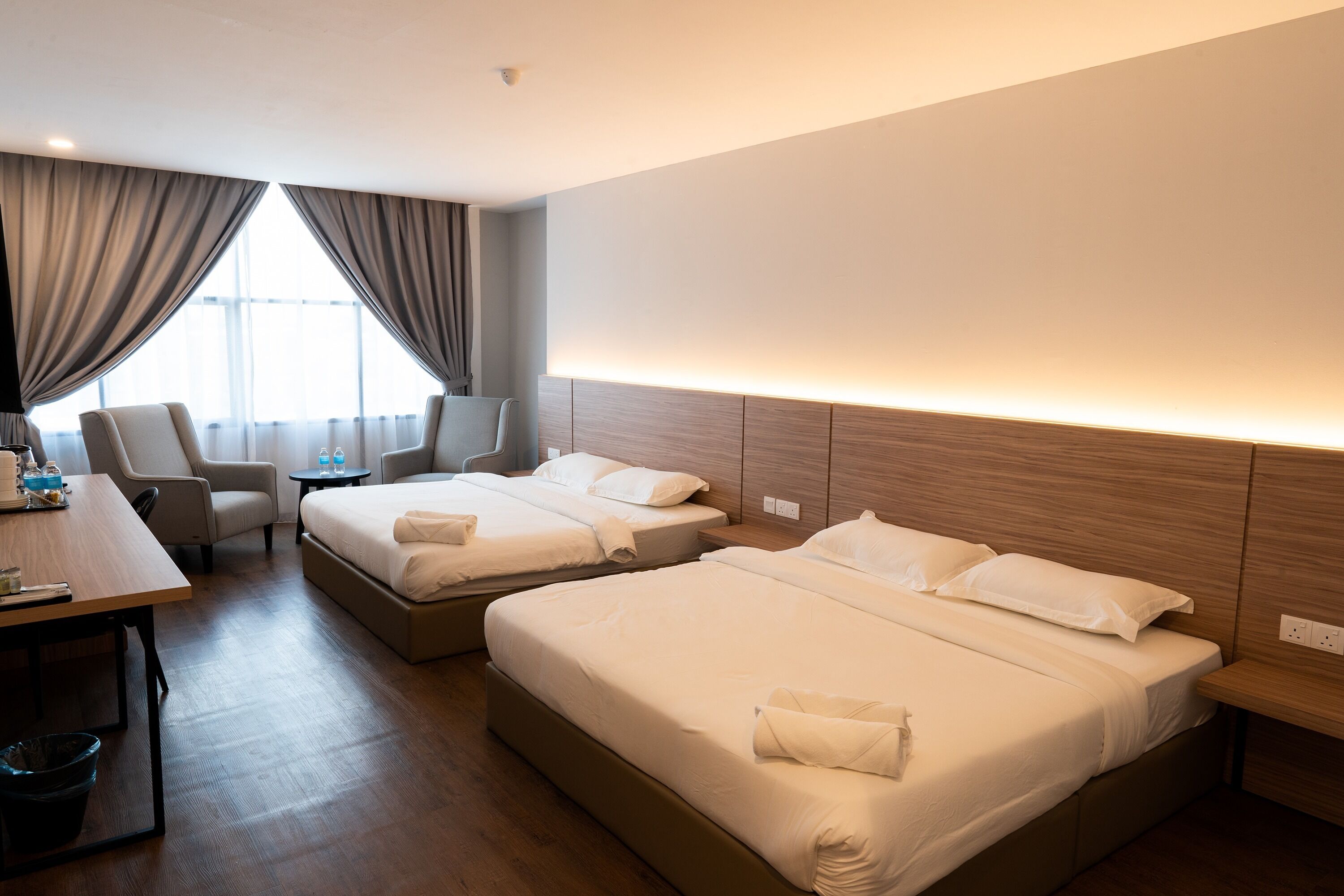 A hotel room with two beds, a desk, a chair, and a view of the outdoors.