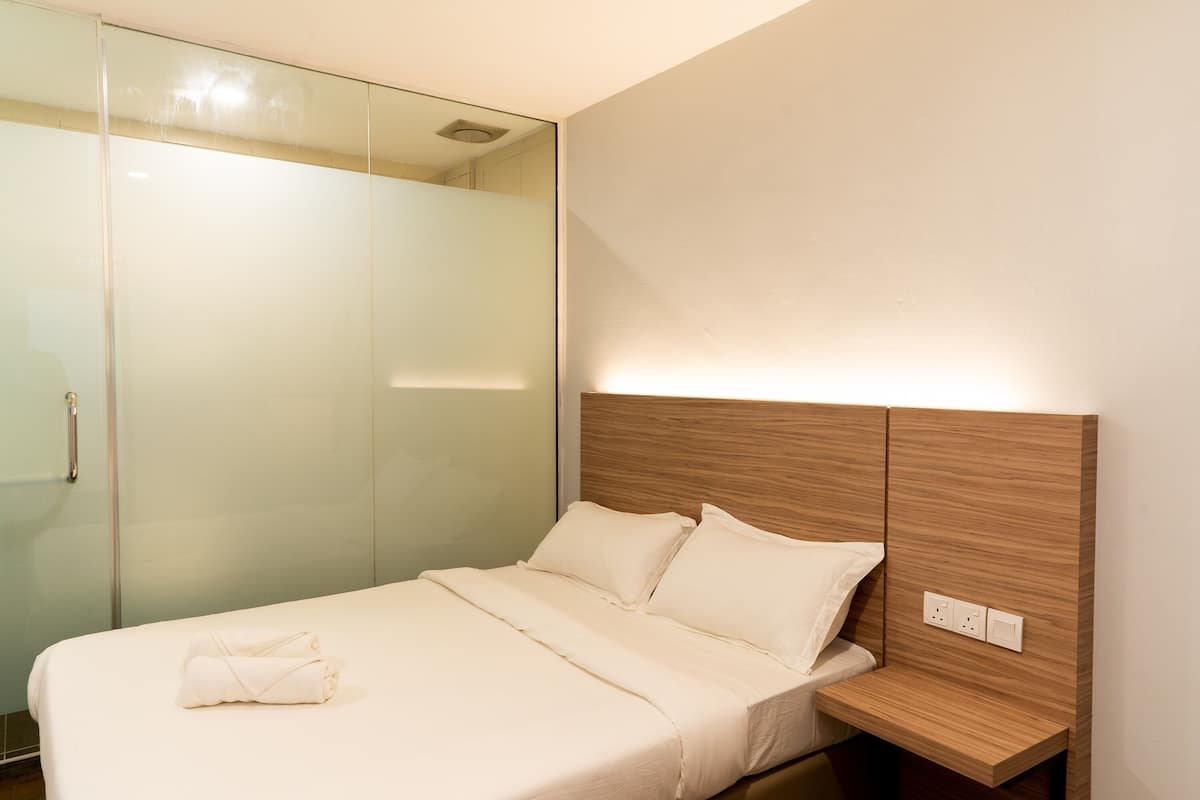 Ein modernes Schlafzimmer mit Glastrennwand, einem Holzkopfende und einem ordentlich bezogenen Bett mit Handtuch.