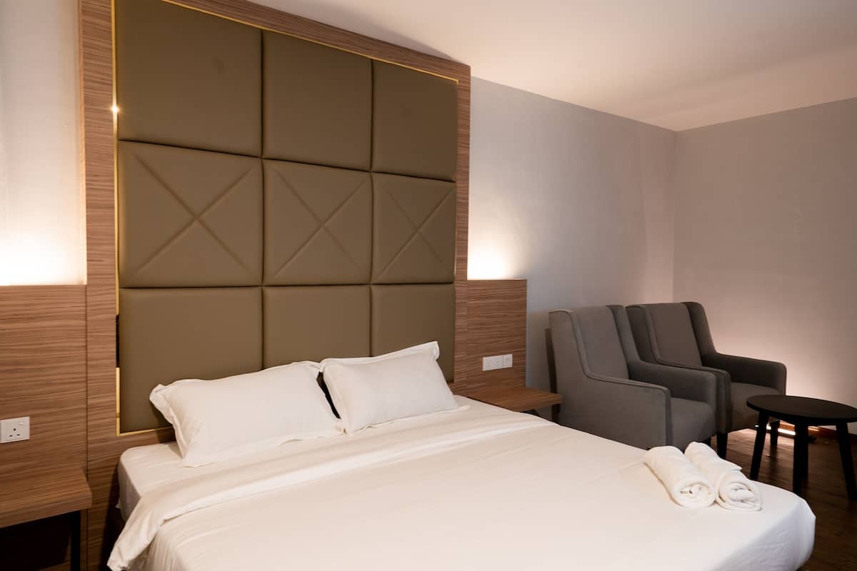 Ein Hotelzimmer mit einem großen Bett, zwei Sesseln, einem kleinen Tisch und einem an der Wand befestigten Kopfteil.