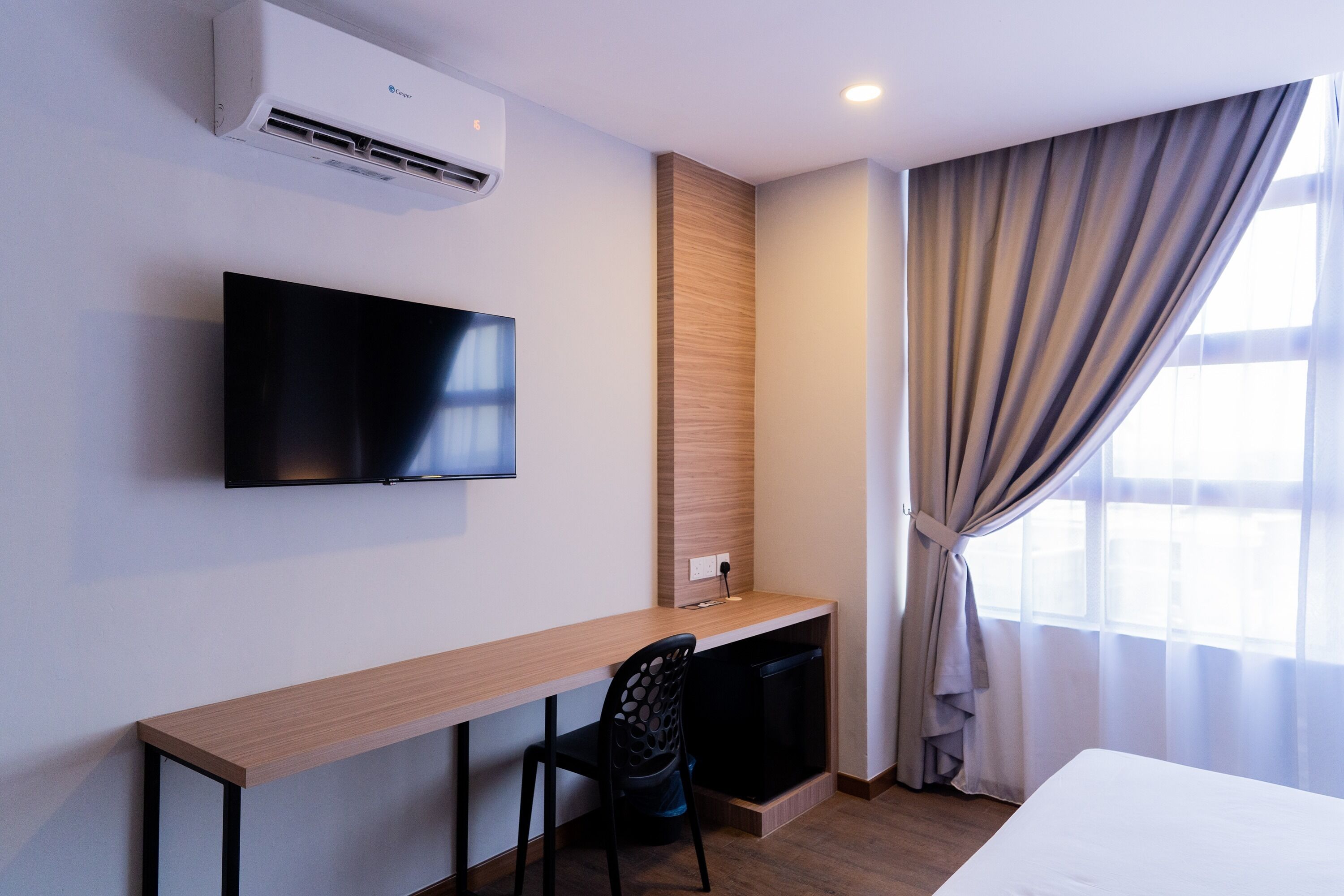 Hotelkamer met een houten bureau, een flatscreen-tv, een ingebouwde airconditioning, een zithoekje en een groot raam met gordijnen.