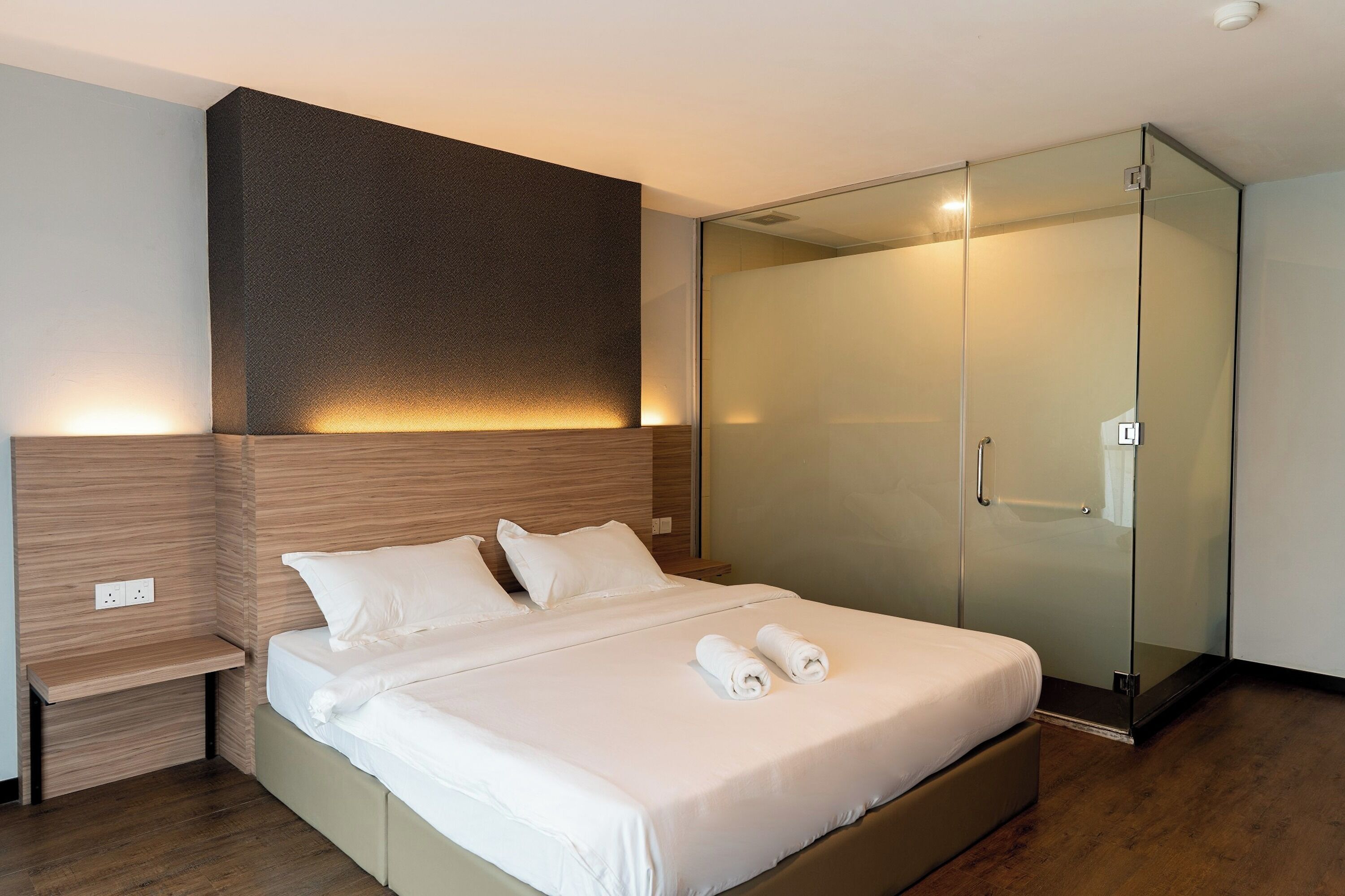 A modern hotel room with a large bed, a glass-enclosed walk-in closet, and a built-in shelf.