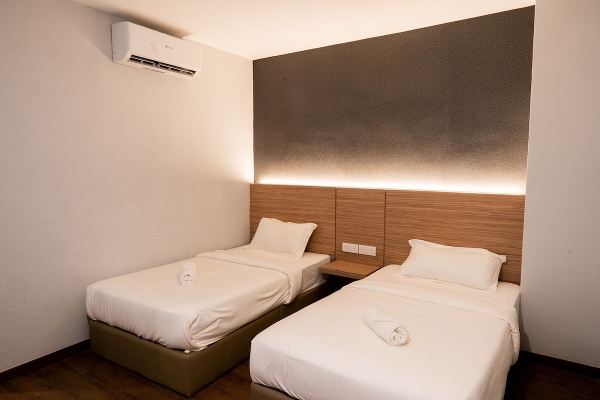 Ein Hotelzimmer mit zwei Einzelbetten, einem Holzkopfteil und einer Klimaanlage.