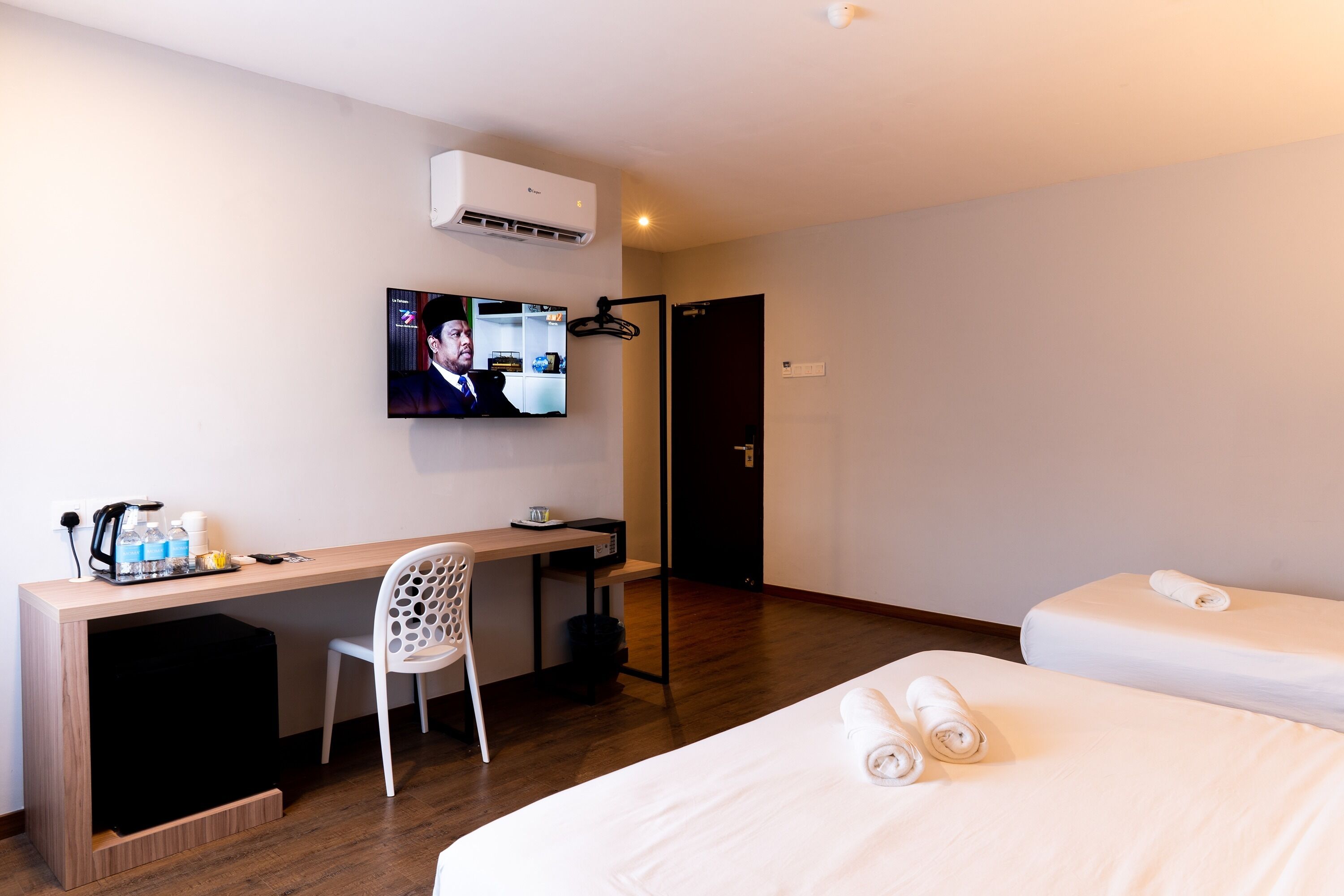 Een hotelkamer met een bureau, stoel, twee bedden, een televisie en een airconditioning.