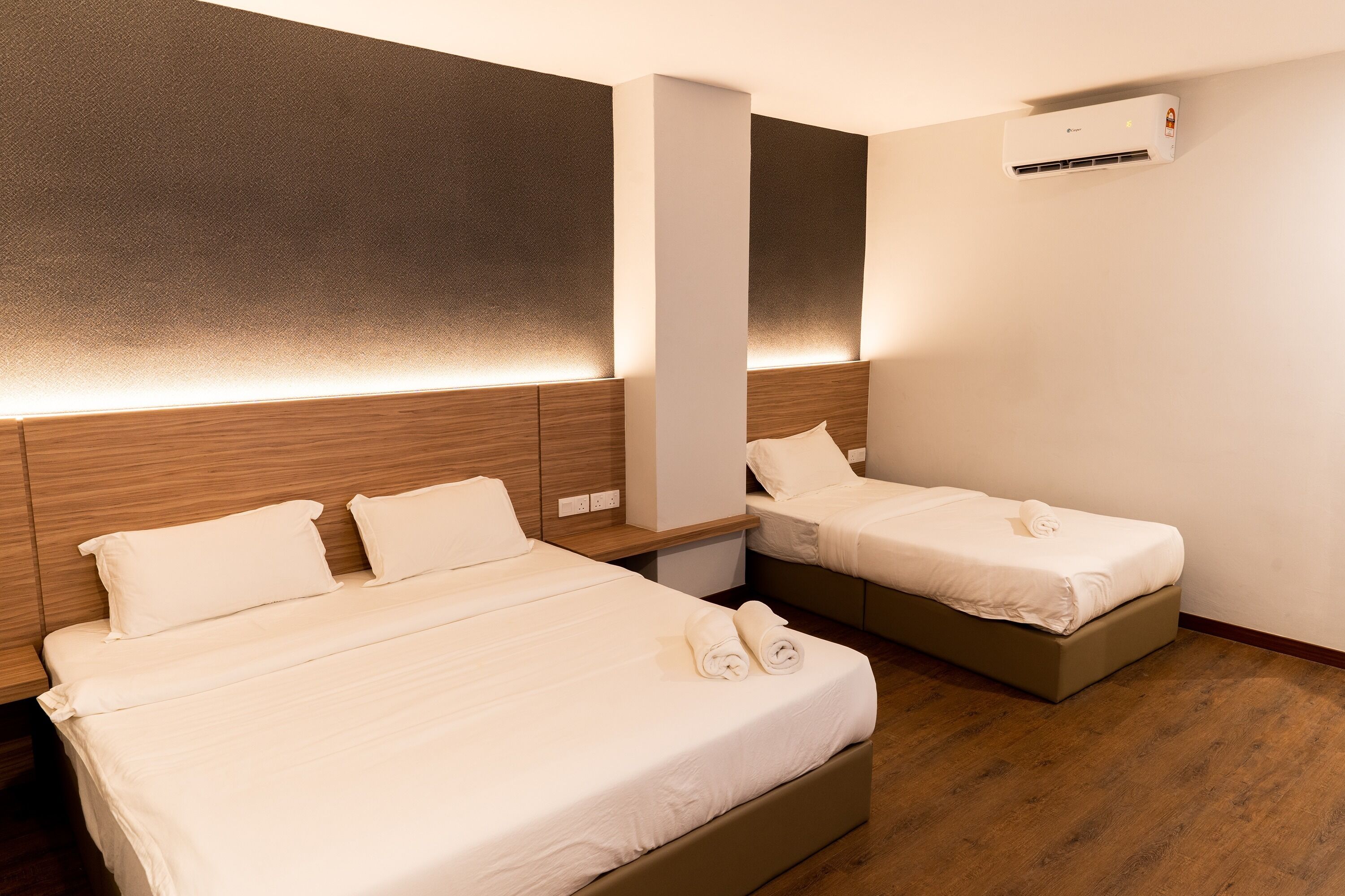 Habitación de hotel con dos camas, cabecero de madera, aire acondicionado de pared y mesita de noche.