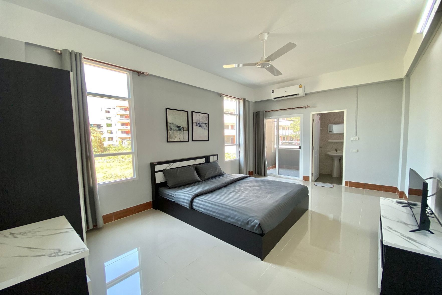 Une chambre moderne avec un lit, un ventilateur de plafond, une salle de bain avec des toilettes et un lavabo, et une grande fenêtre.