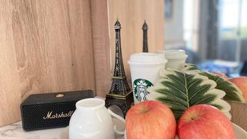 A table with a white teapot, a black box labeled "Marshall," two Eiffel Tower figurines, a Starbucks cup, and a bowl of apples.