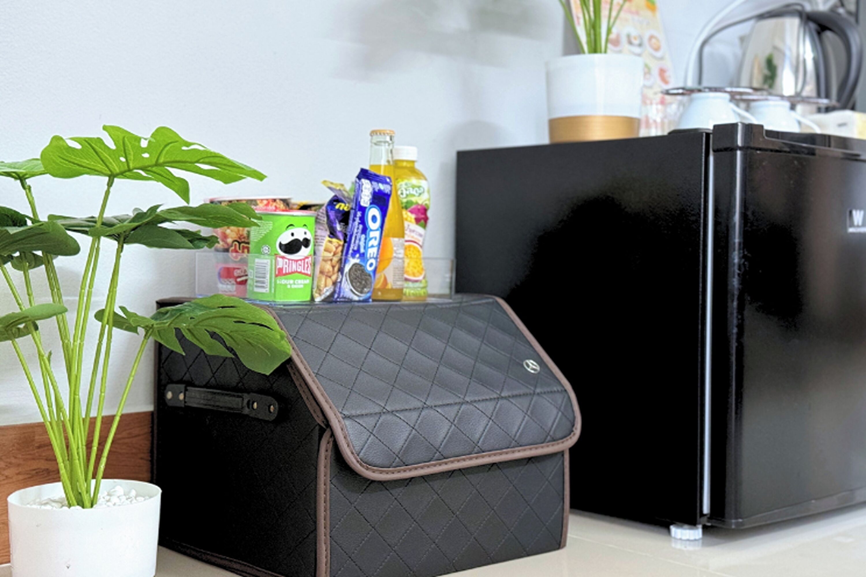A kitchen area with a black refrigerator, a black suitcase with a quilted cover, and a potted plant.
