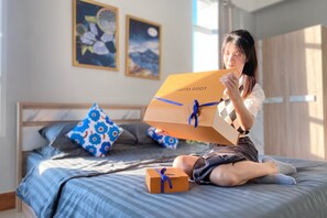 Une personne assise sur un lit, à côté d’une boîte Louis Vuitton et d’une plus petite boîte cadeau.