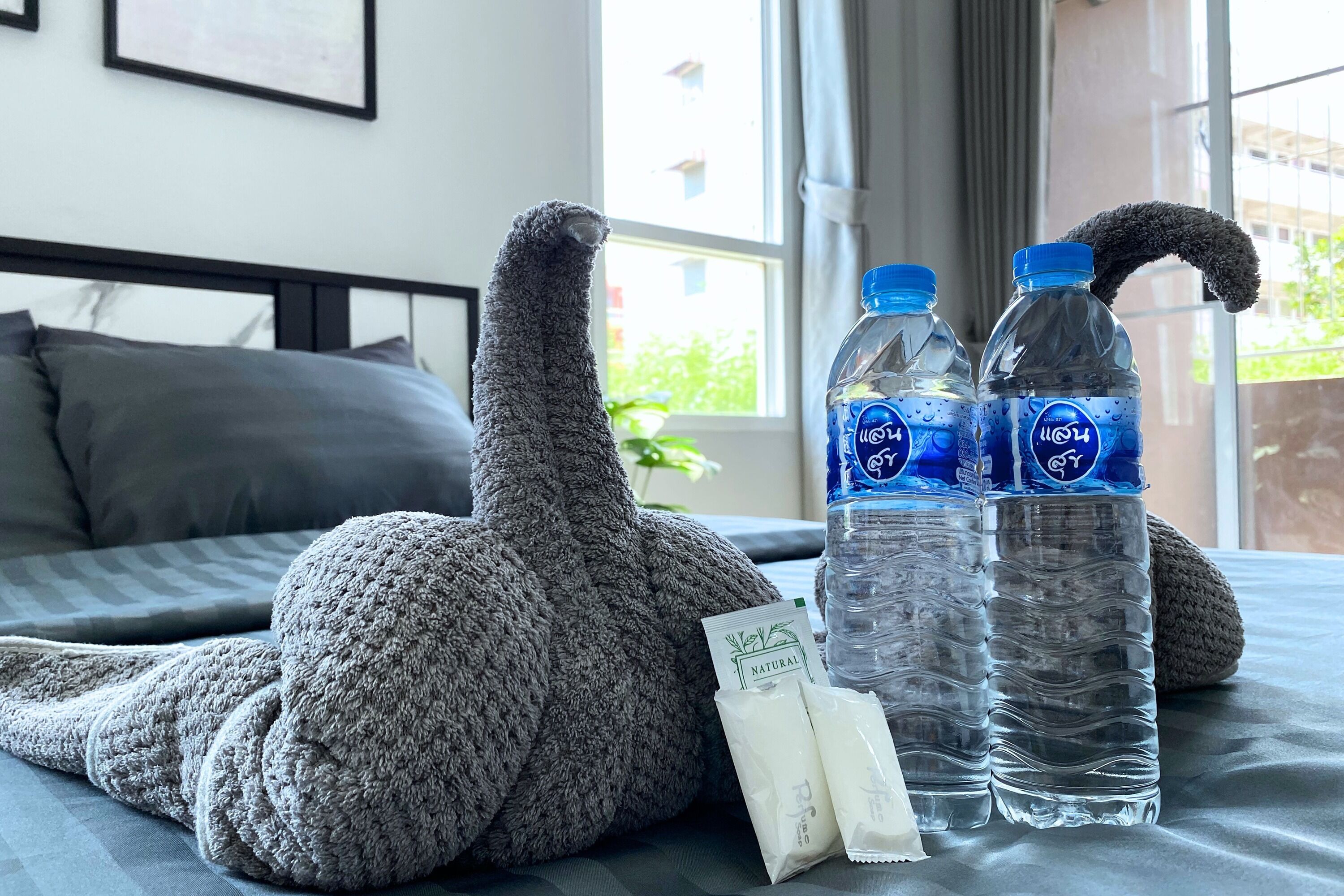A bed with a gray knitted blanket, two water bottles, and a packet of tissues.