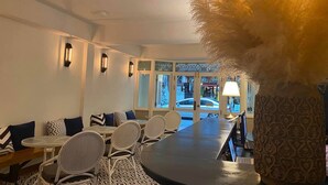 A modern dining area with a long table and chairs, a sofa with patterned cushions, and a decorative vase. - Forgotten Hostel Silom (Bangkok)