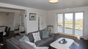 En moderne stue med en grå sofa, et hvidt sofabord og et spiseområde med et hvidt bord og stole.