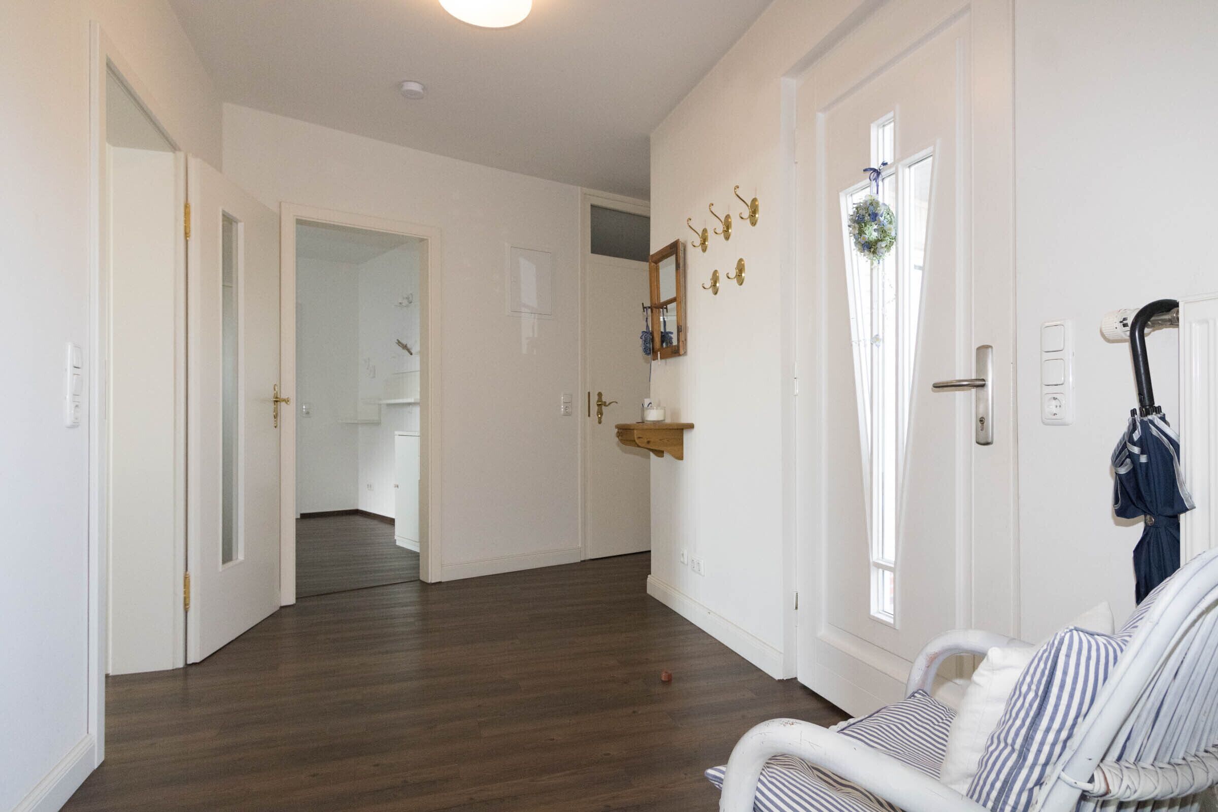 A hallway with a wooden floor, white walls, and a door leading to a bathroom.