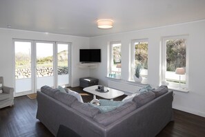 A modern living room with a gray sectional sofa, a white coffee table, and a flat-screen TV mounted on the wall.
