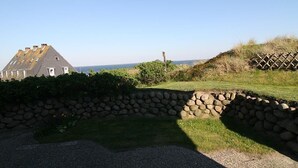 En stenvæg, et græsareal og en bygning med saddeltag.