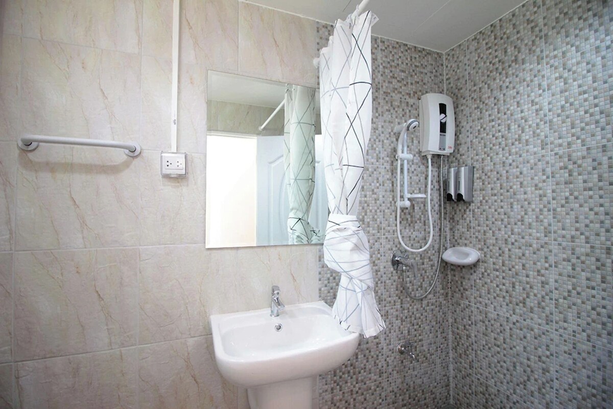 Bagno con lavandino bianco, uno specchio, doccia con parete piastrellata e mancorrente.