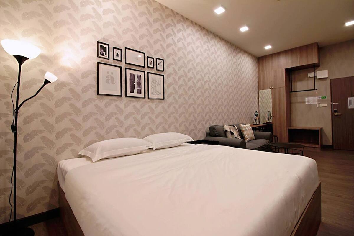 A hotel room with a large bed, a desk, a chair, a lamp, and framed pictures on the wall.