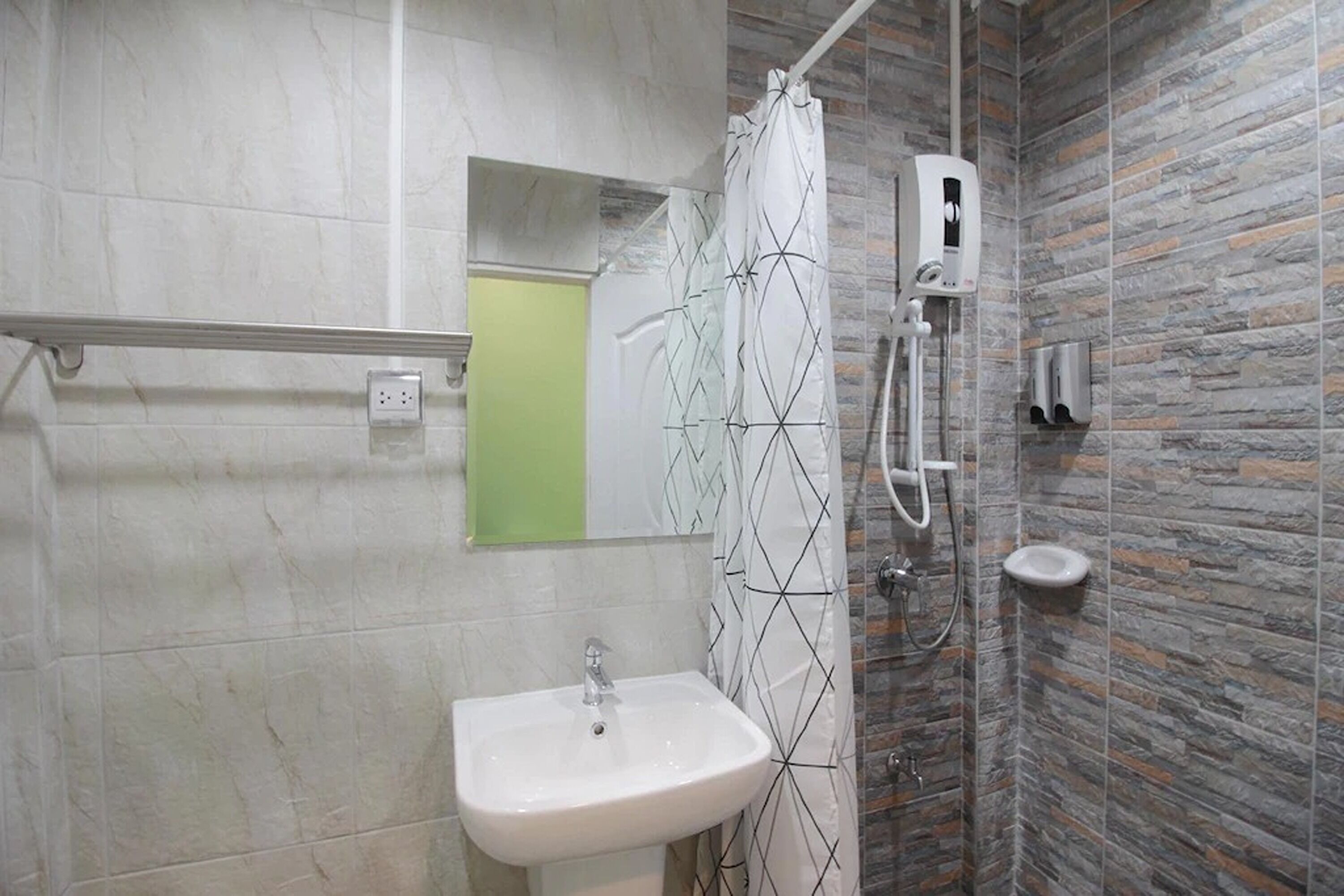 Ein Badezimmer mit einem weißen Waschbecken, einem Spiegel, einer Dusche mit gemustertem Vorhang und einer Wand mit Steinoptik.