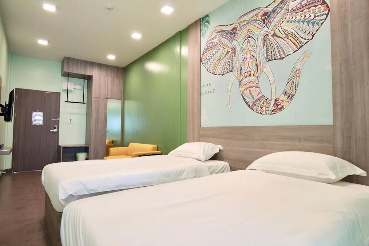 A hotel room with two beds, a large wall mural of an elephant, and a wooden wardrobe.