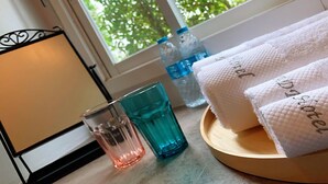 A window with a view of trees, a wooden tray with white towels, and two glasses on a table. - R 17 Living Hotel (Bangkok)