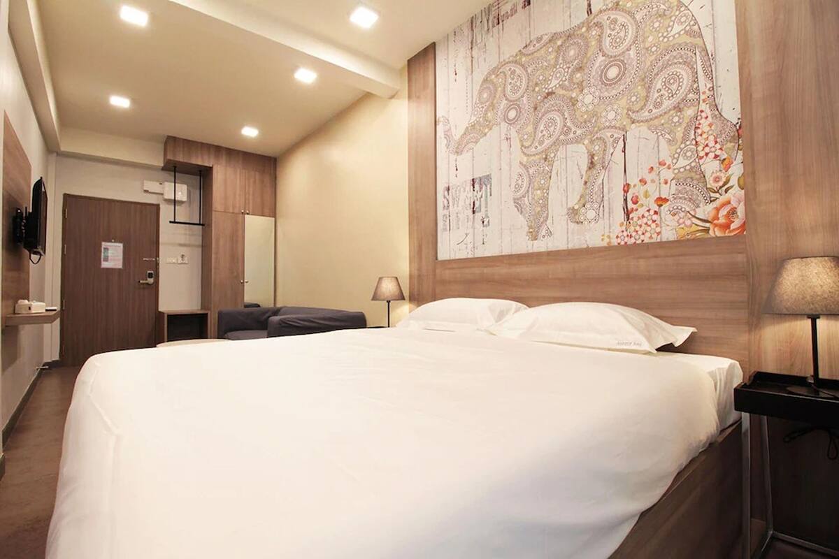 A hotel room with a large bed, a wooden headboard, a wall-mounted TV, and a decorative elephant tapestry.