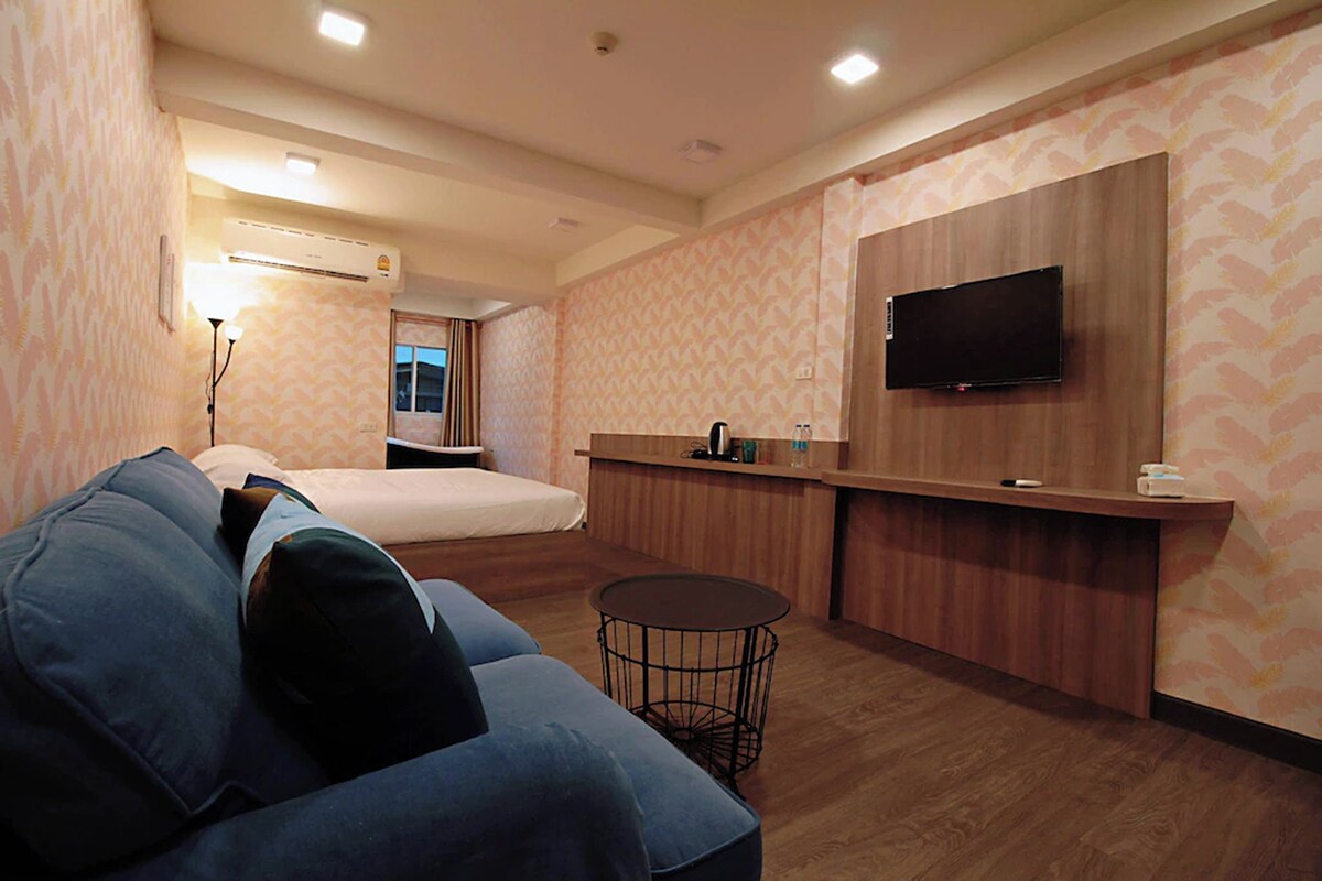 Una camera d'albergo con un letto, una poltrona, un tavolino rotondo, una televisione a parete e un bancone in legno.