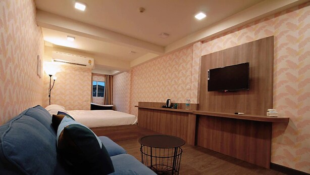 A hotel room with a bed, a sofa, a small round table, a TV mounted on the wall, and a wooden counter. - R 17 Living Hotel (Bangkok)