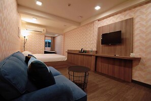 A hotel room with a bed, a sofa, a small round table, a TV mounted on the wall, and a wooden counter. - R 17 Living Hotel (Bangkok)