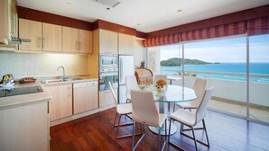 A modern kitchen with a dining area, large windows, and a view of the sea. - Patong Tower Beach Apartment By Seesea (Patong)