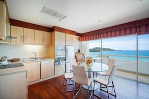 A modern kitchen with a dining area, large windows, and a view of the sea.