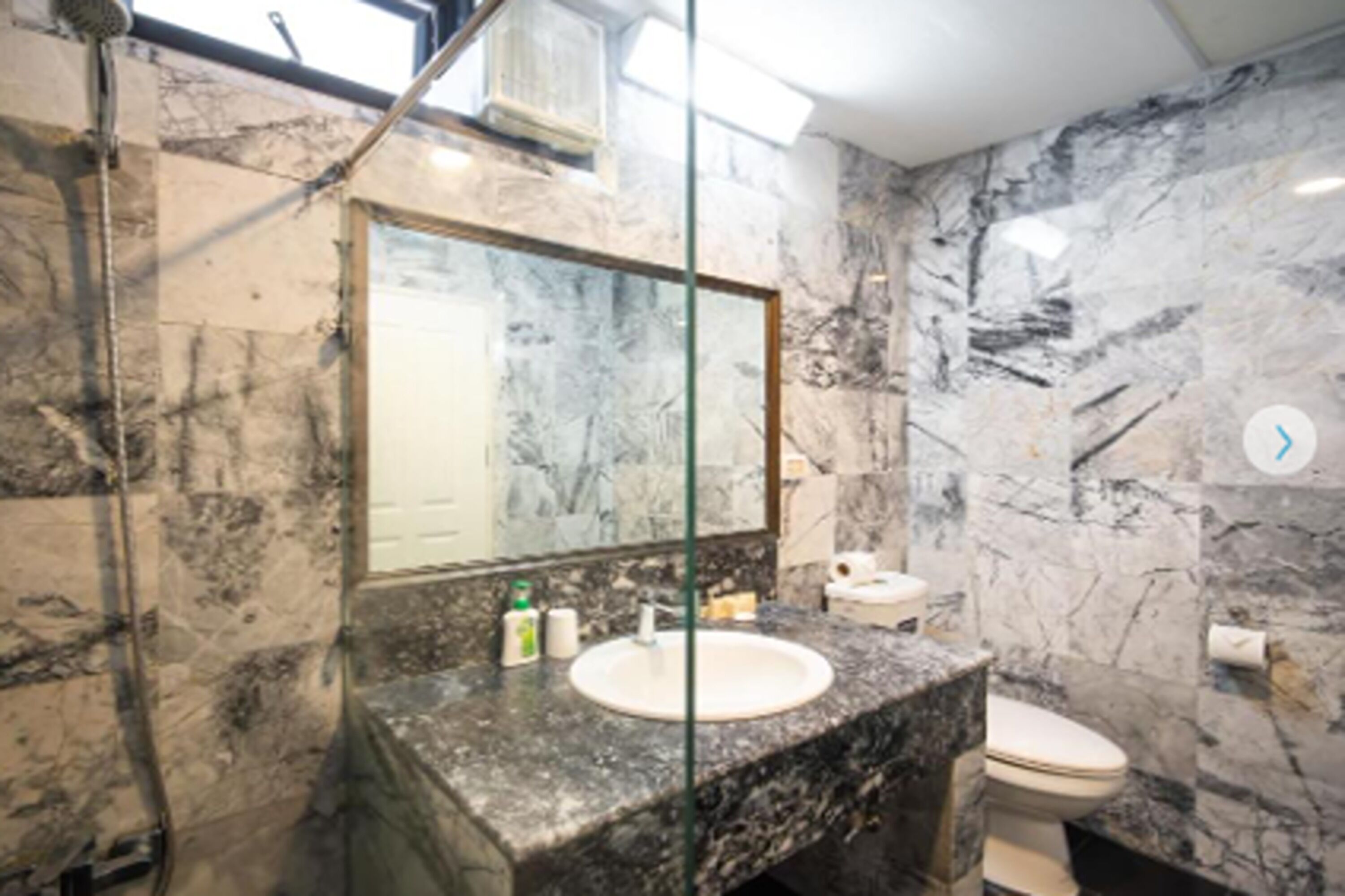 A bathroom with a marble sink, a toilet, and a glass shower enclosure.