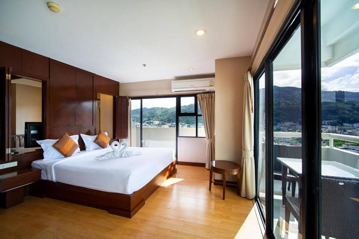 A modern hotel room with a large bed, a desk, and a balcony with a city view.