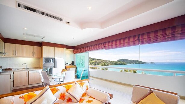 A modern hotel room with a balcony, a kitchen area, and a bed with floral bedding. - Patong Tower Beach Apartment By Seesea (Patong)