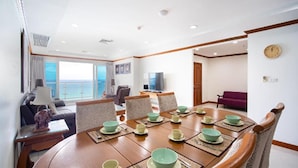 A dining area with a round table set for four, surrounded by chairs. There is a television on a stand in the background, and a sofa is visible in the adjacent room. - Patong Tower Beach Apartment By Seesea (Patong)