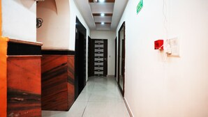 A hotel hallway with a reception desk, a staircase, and a door with a circular window design. - Hotel Le Sancy (New Delhi)