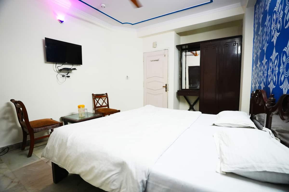A bedroom with a bed, a chair, a small table, a TV mounted on the wall, and a wardrobe.