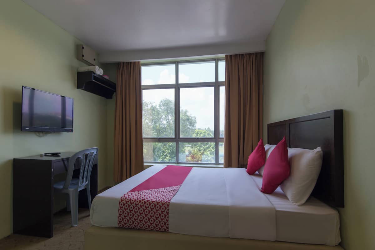 A hotel room with a bed, a desk, a chair, a television, and a window with curtains.